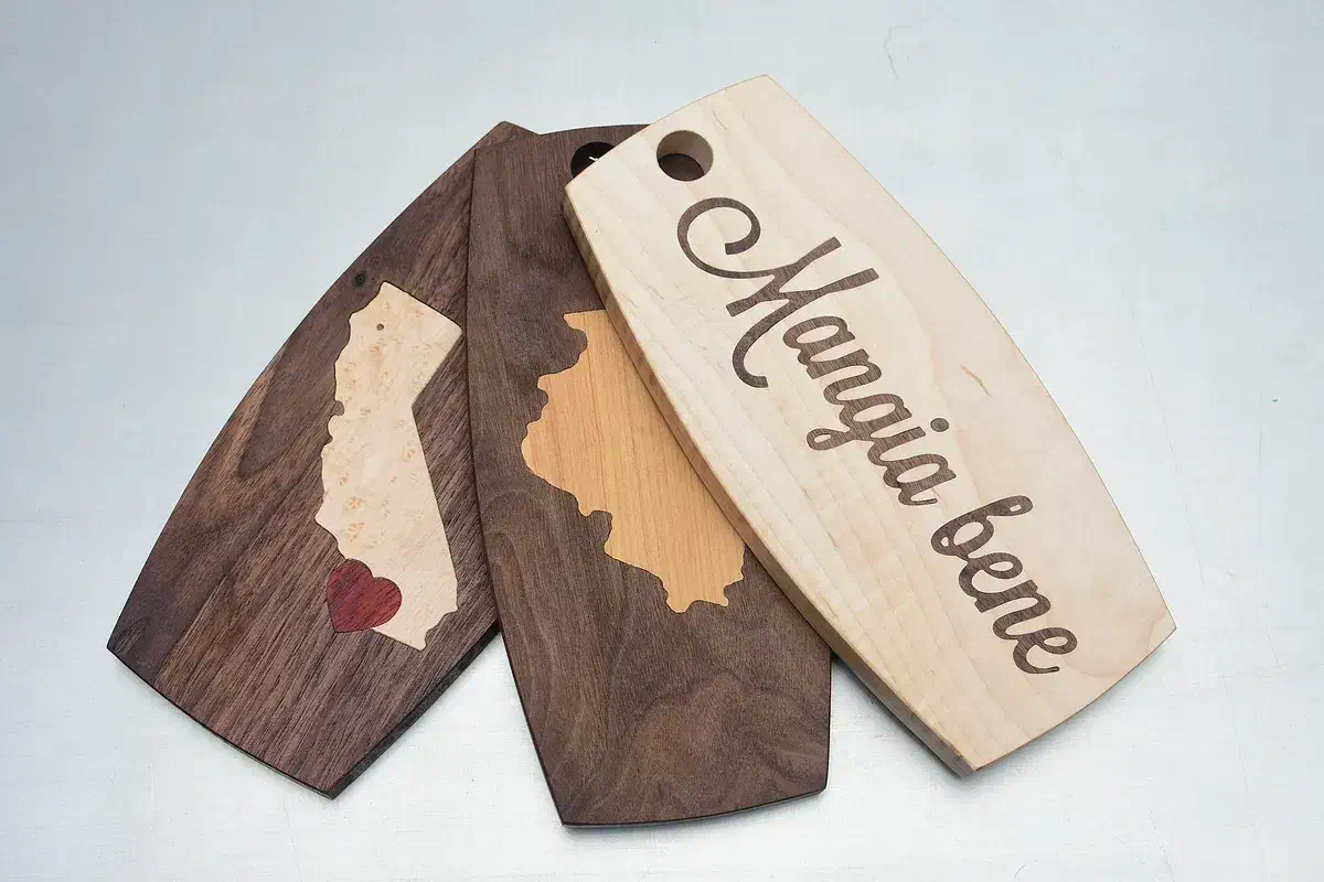 A finished wooden handled cutting board with pale lettering inlaid in the face