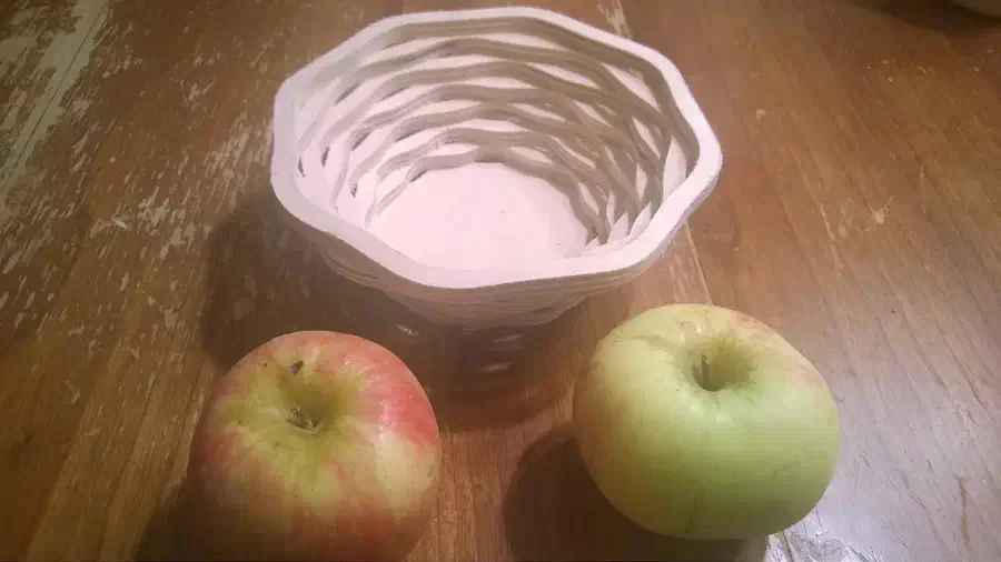 An open-sided wooden bowl built from scalloped rings beside two apples
