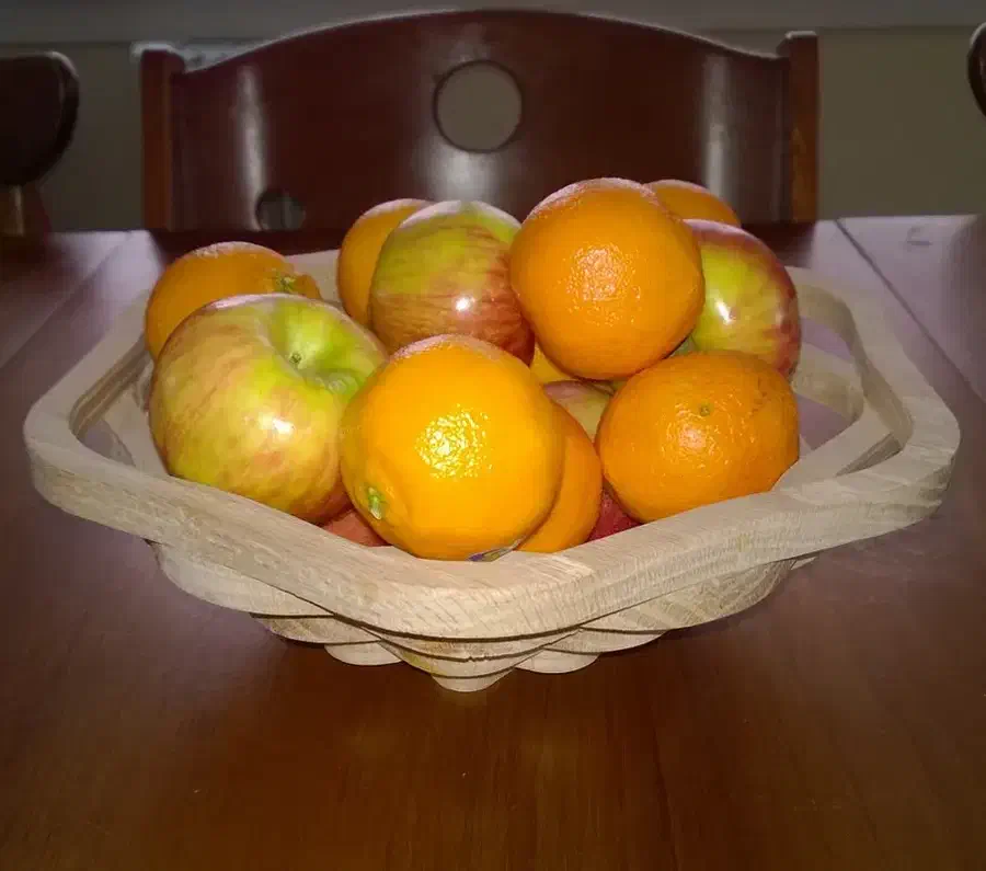 A stacked wooden bowl holding oranges and apples on a dark table