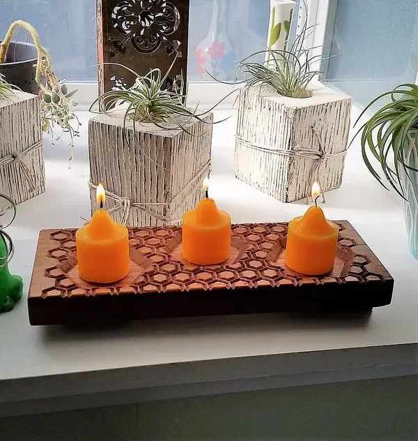 A rectangular wooden holder with honeycomb carving and three orange candles on a windowsill