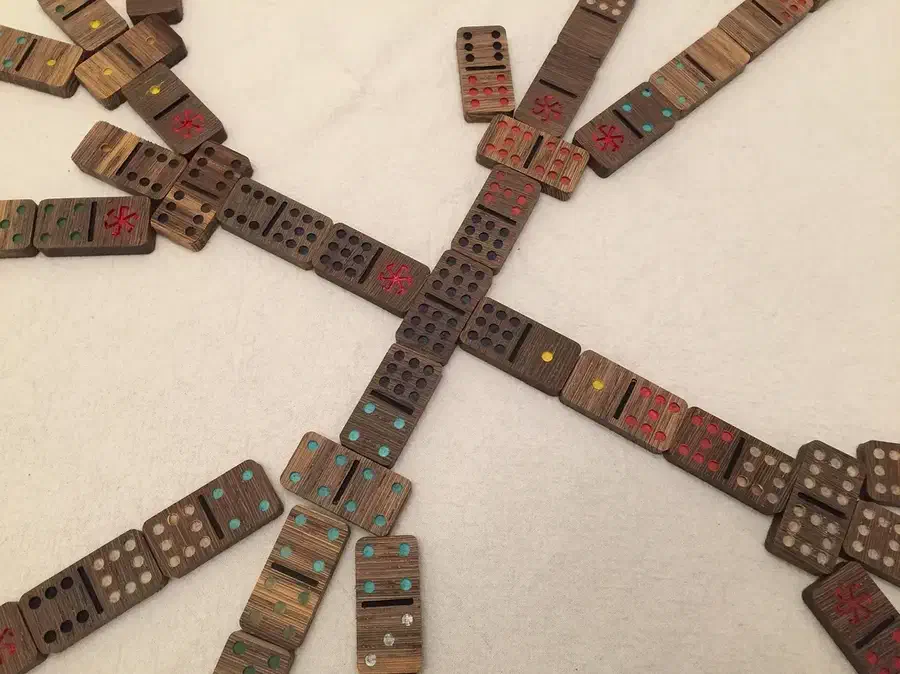 Painted wooden dominoes with colored pips and red spinner symbols arranged in a game on a pale tabletop