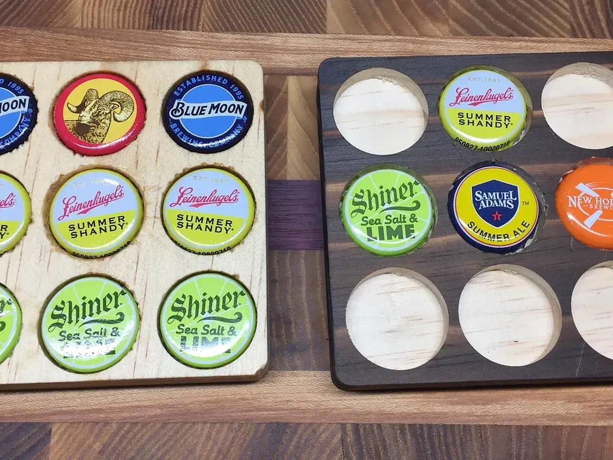 Two square wooden coasters with gridded cap pockets, one filled with colorful beverage caps and one partly filled