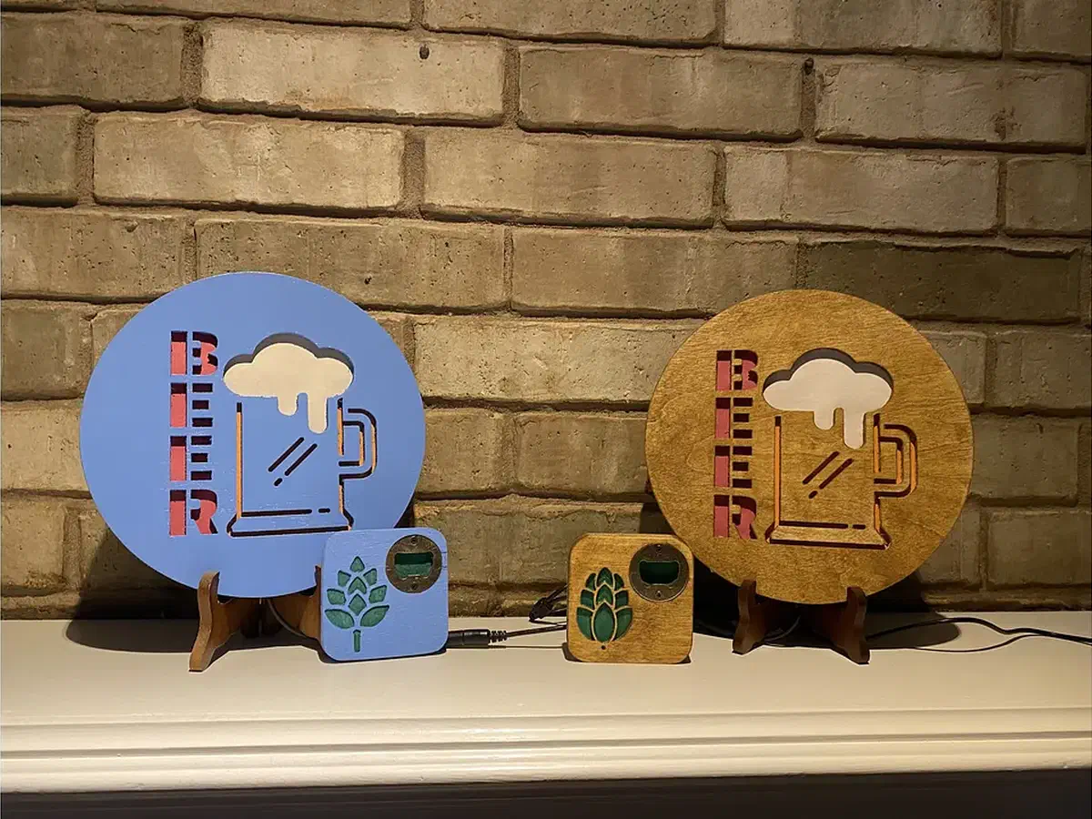 Finished blue and natural-wood coaster bottle openers with metal inserts beside matching illuminated beer signs