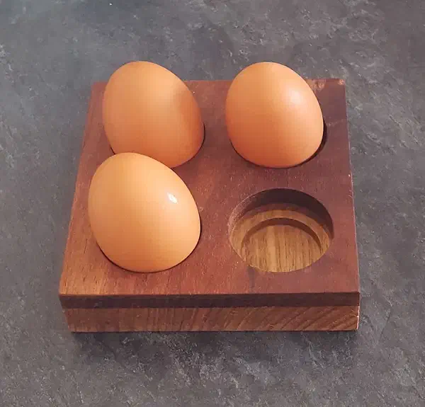 Three eggs beside an empty recess in a square holder made from contrasting timber layers