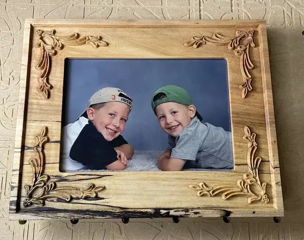 A carved wooden picture frame with floral corners holding a photograph of two children