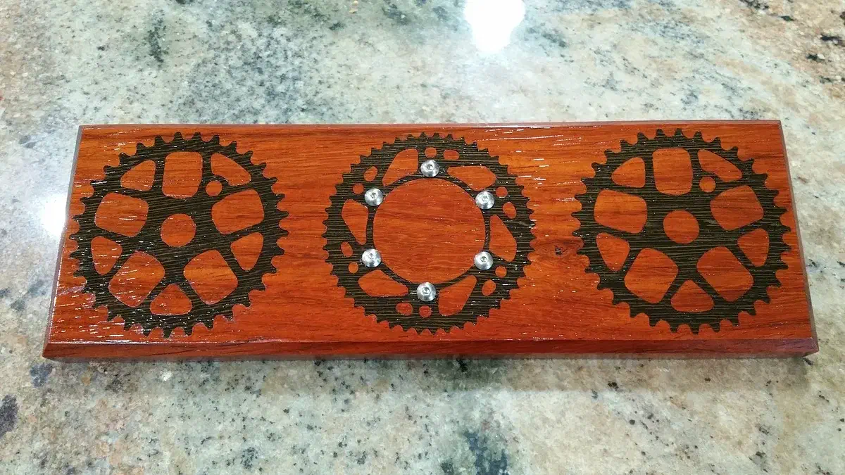 Finished reddish wooden key holder with three dark bicycle gears and six small metal magnets in the center gear