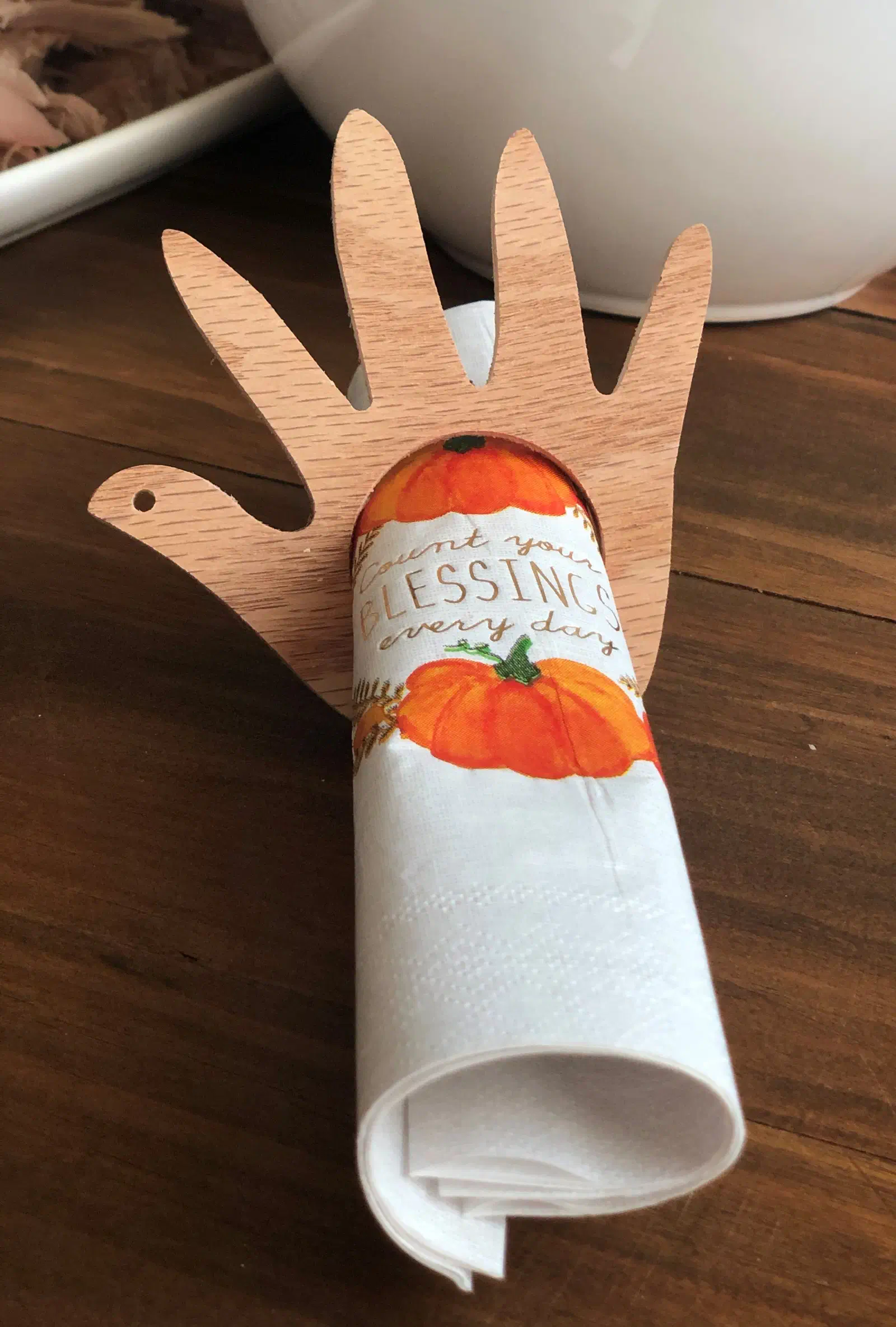 A hand-shaped wooden turkey napkin ring holding a rolled white napkin on a wooden table