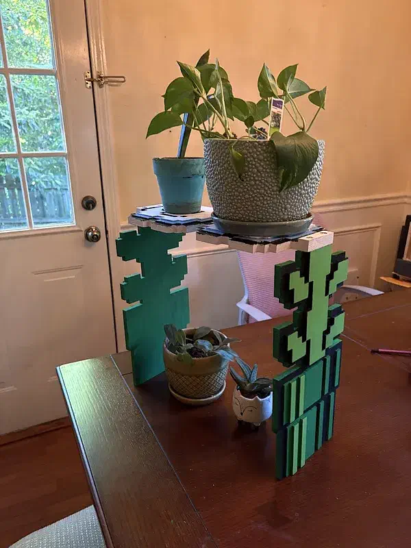 Two plant pots on a green painted pipe-and-vine wooden shelf on a desk