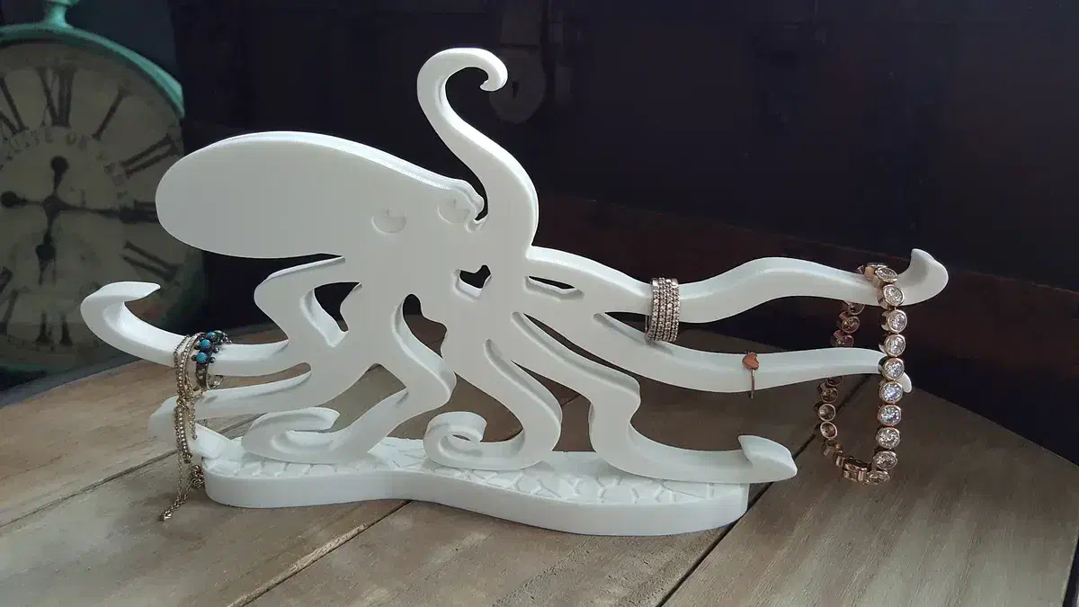 A white Corian octopus standing on a patterned base with rings and a chain on its arms
