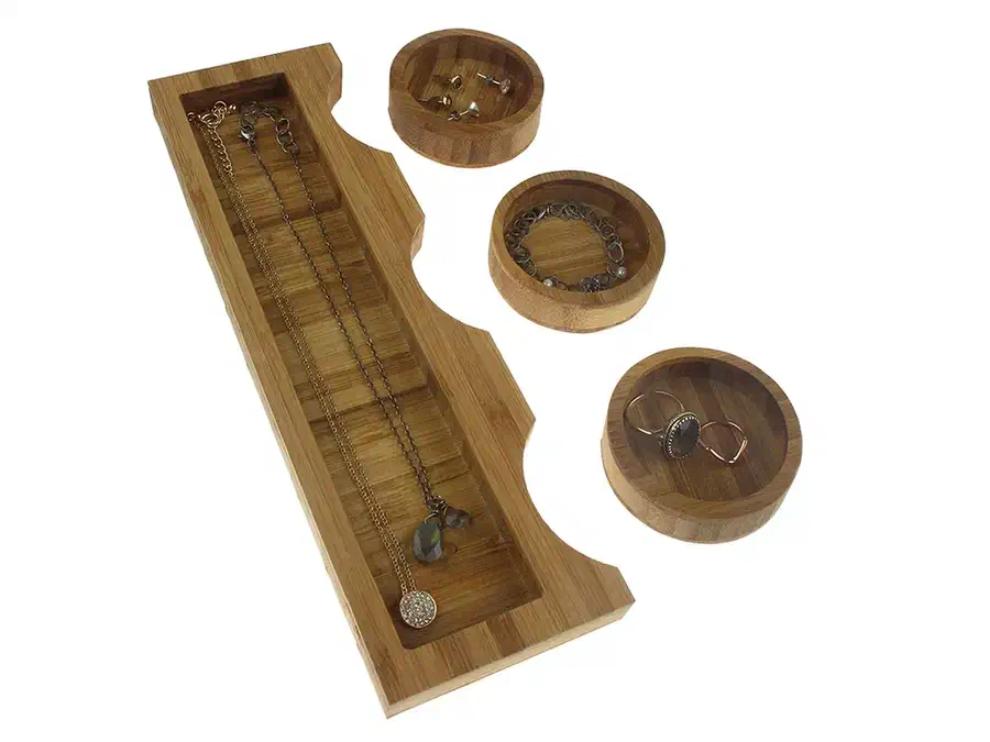 A bamboo tray beside three removable round bowls holding rings, earrings and a bracelet