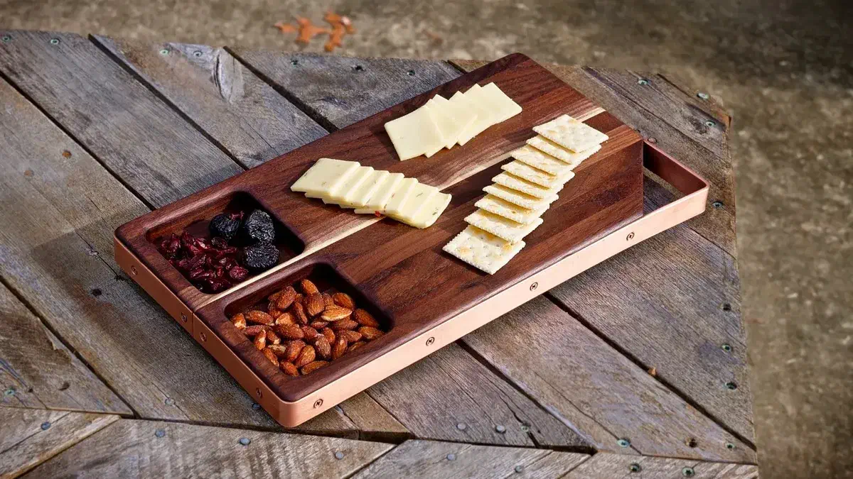 A walnut serving board with copper-colored edging, cheese, crackers and nuts