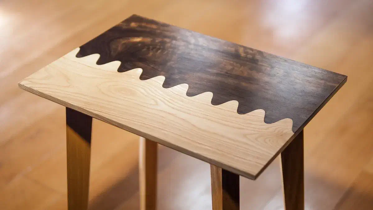 A small wooden side table with light and dark boards meeting along a wavy joint