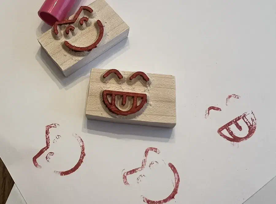Two small wooden face stamps beside red printed impressions on white paper