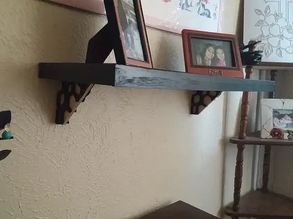 A dark wooden wall shelf supported by open geometric brackets and holding framed photographs