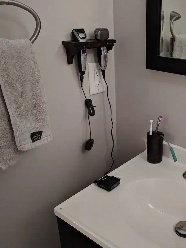 A wall-mounted wooden razor shelf beside a bathroom mirror, holding a razor and trimmer above the sink