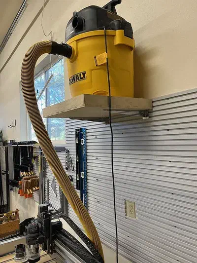 A yellow shop vacuum resting in a plywood tray on metal wall brackets
