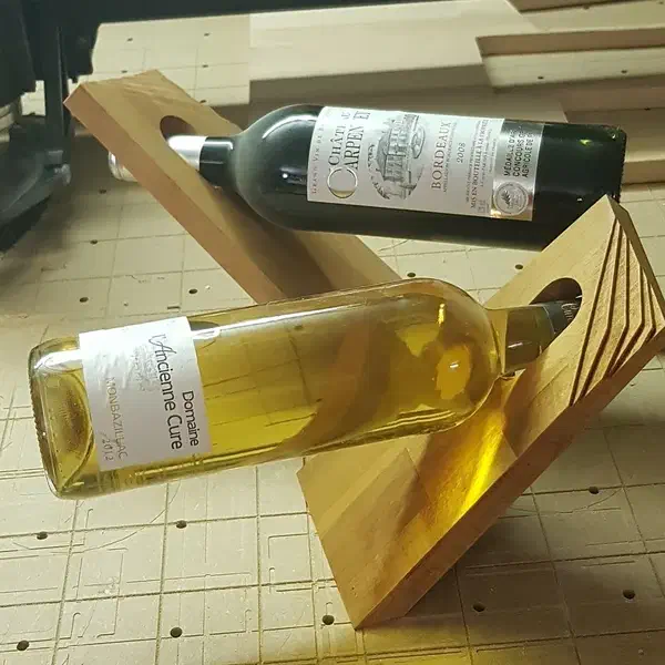 Two wooden balancing bottle holders supporting bottles on a workbench, one with an animal carving