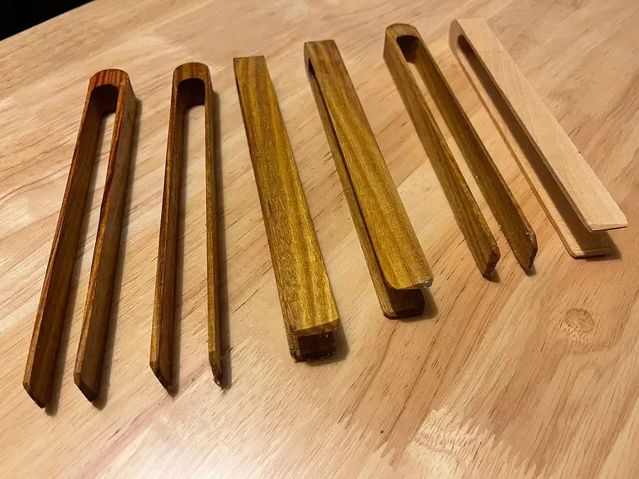 Finished wooden toaster tongs in several wood colors laid out on a wooden countertop