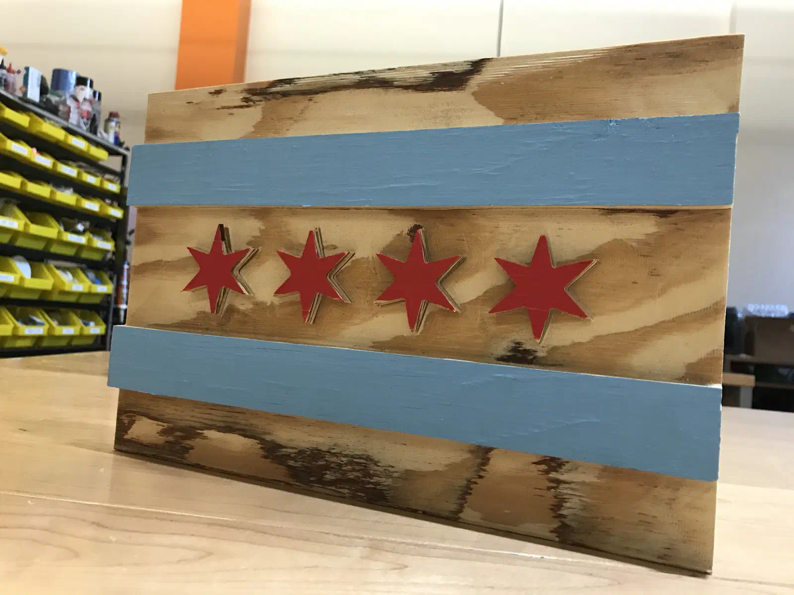 A Chicago flag carved into a wooden board, with two blue stripes and four red stars.